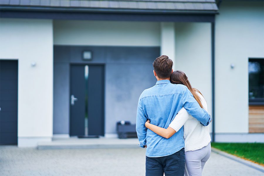 Insurance Quote - Back View of a Young Couple Hugging Each Other While Standing Outside Looking at Their New Home